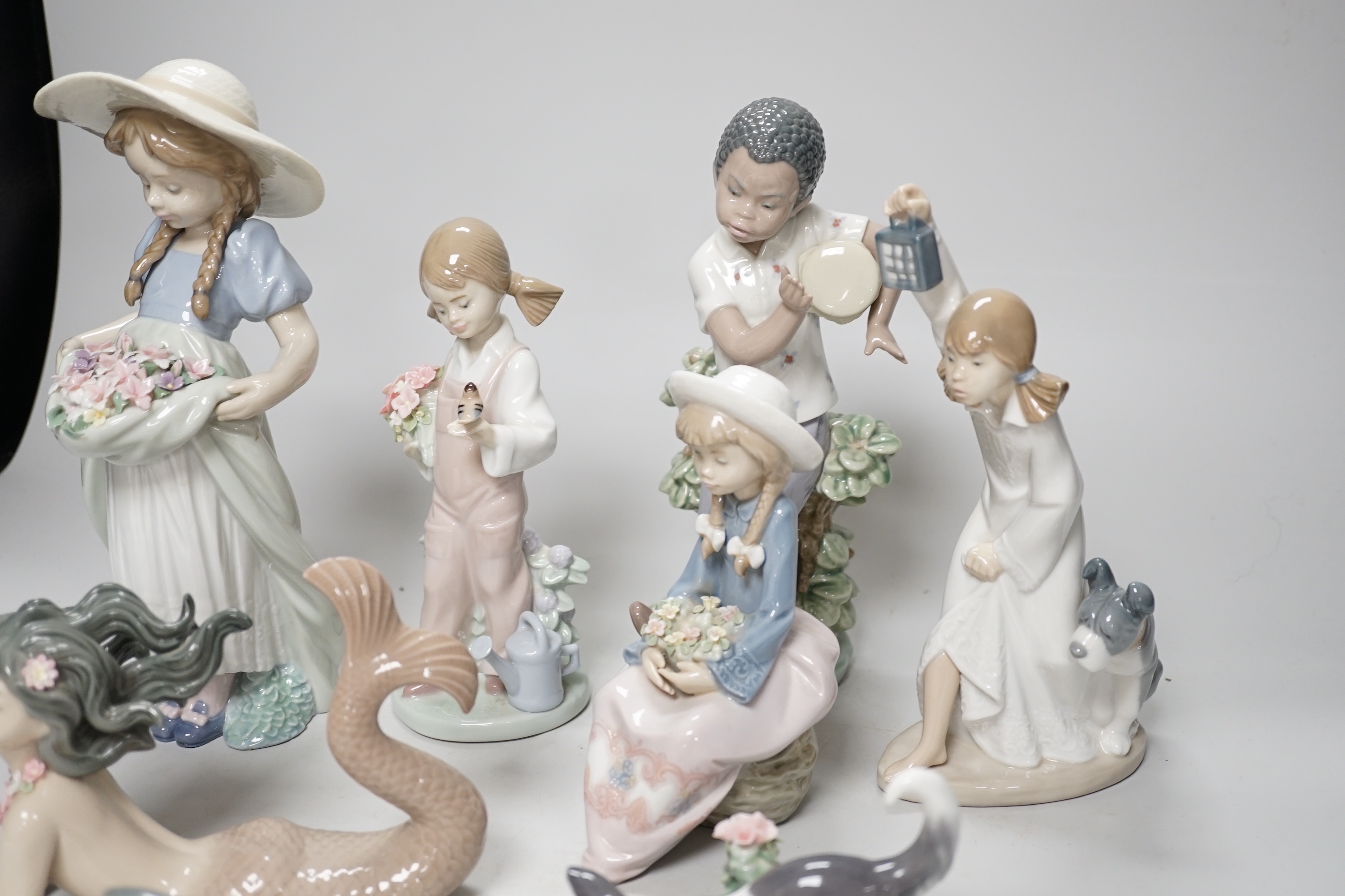 A large Lladro figure of a flower girl, mermaid, boy playing a drum and five other models including a Nao example, the largest 24cm high (8)